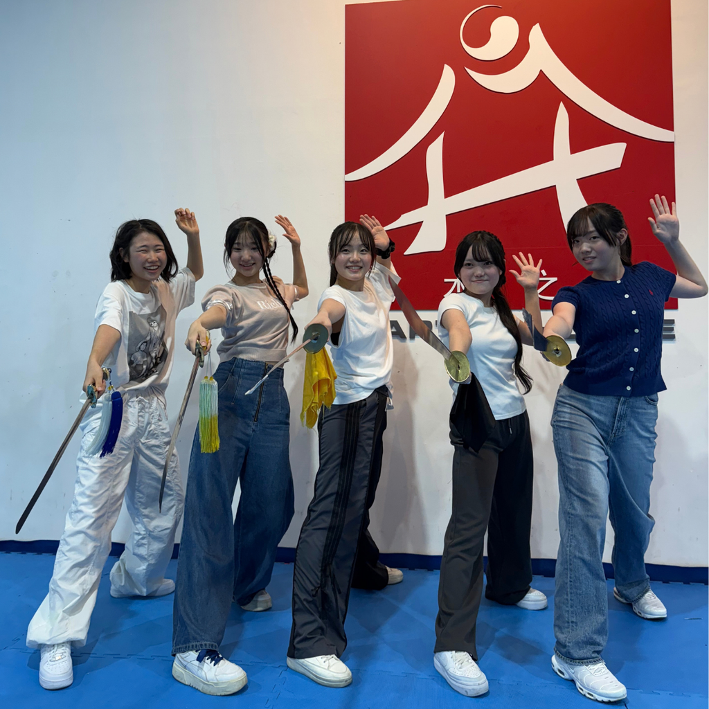 A group of Japanese students striking a pose with the swords and broadswords at the Wushu introductory workshop